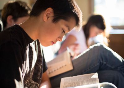 Young Asian boy reading scriptures with other kids in the background also reading