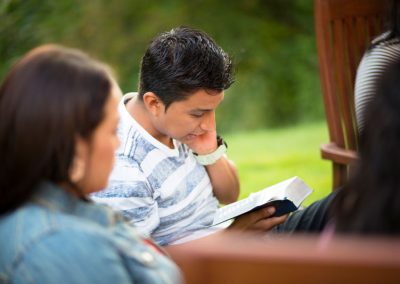 Young adult sitting outside reading scriptures with an older lady in the foreground