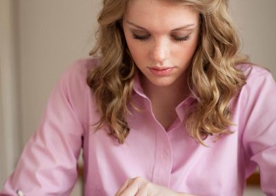 Blonde young woman in a pink collared shirt reading scriptures at a table and writing in a notebook